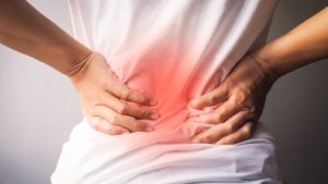back view of person wearing a white t-shirt holding back with the affected region highlighted in red. What Is a nerve root block & How can it help my lower back pain?