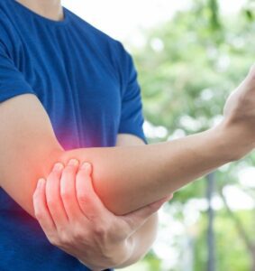close-up of a person in a blue t-shirt holding hands with the affected area highlighted in red. He is need of an arm specialist.