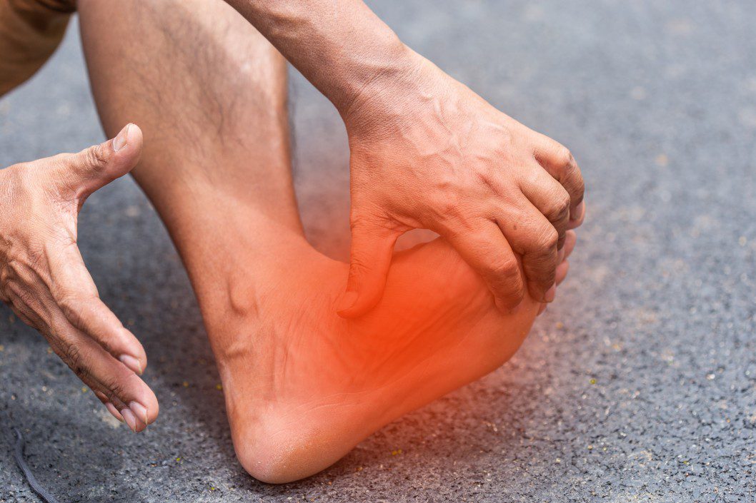 close-up of a person holding his foot due to pain with the affected region highlighted in red. He is need of a foot pain specialist.