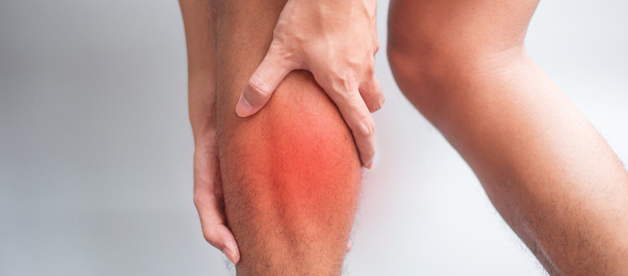 close-up of a man holding calf in pain with the affected region highlighted in red on a white background. He is in need of a leg pain specialist.