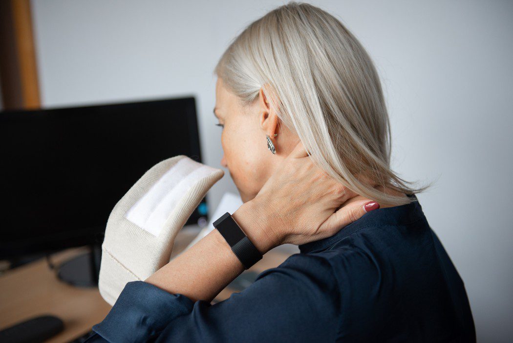 lady with blonde hair in a dark blue blouse holding her neck in pain