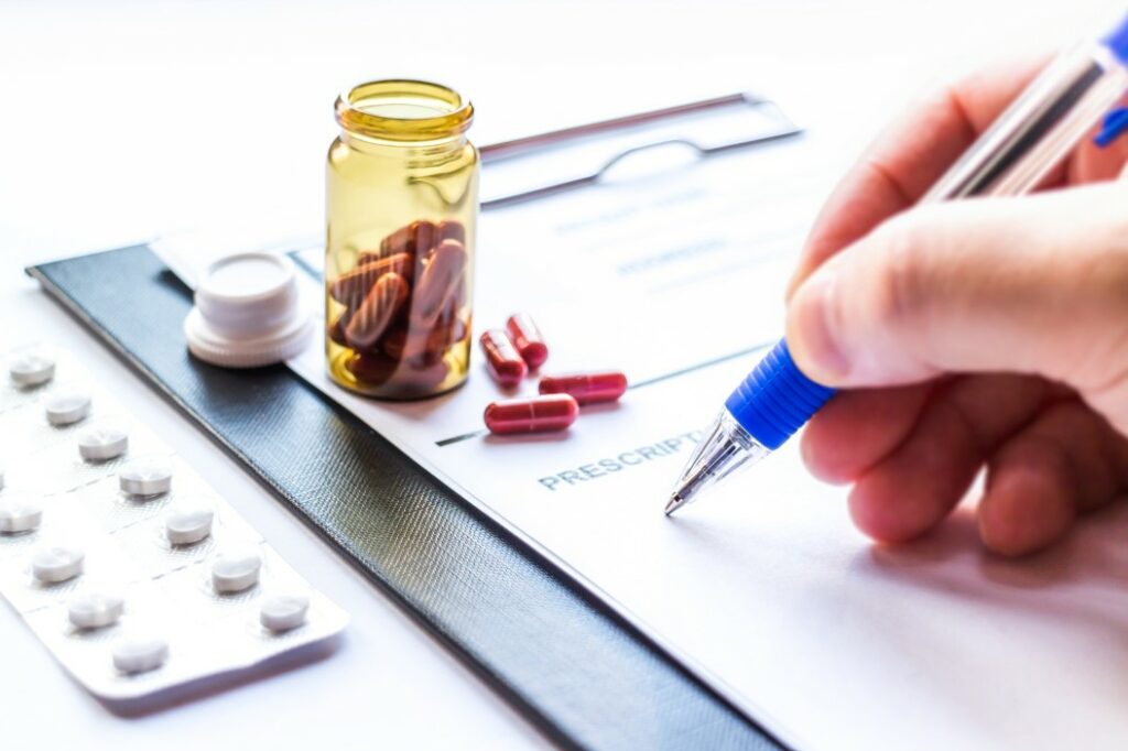 close-up of a person writing on a piece of paper on a black clipboard with a blue pen next to a jar of prescription medication