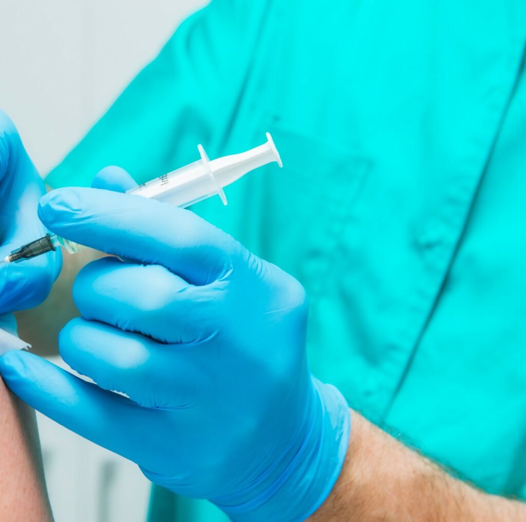 doctor in blue uniform and blue gloves injecting needle to a patient's shoulder