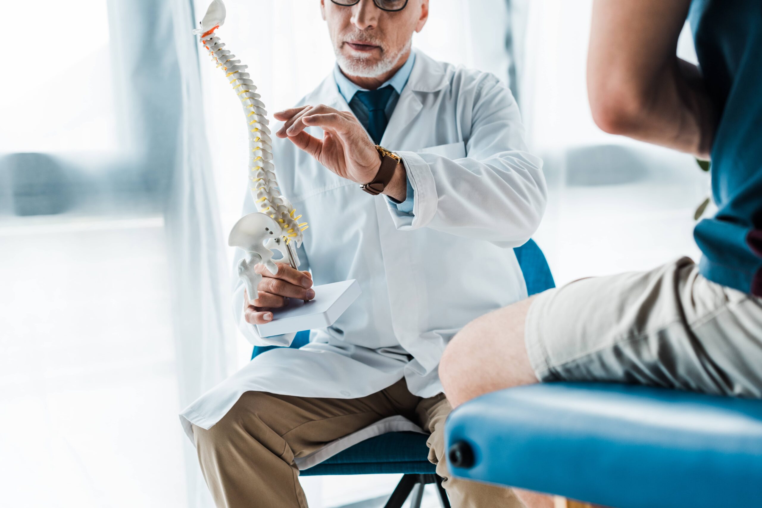 doctor holding a spine model while gesturing with his hands